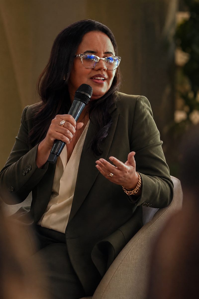 Maristela Oliveira sentada, com microfone na mão, durante uma palestra